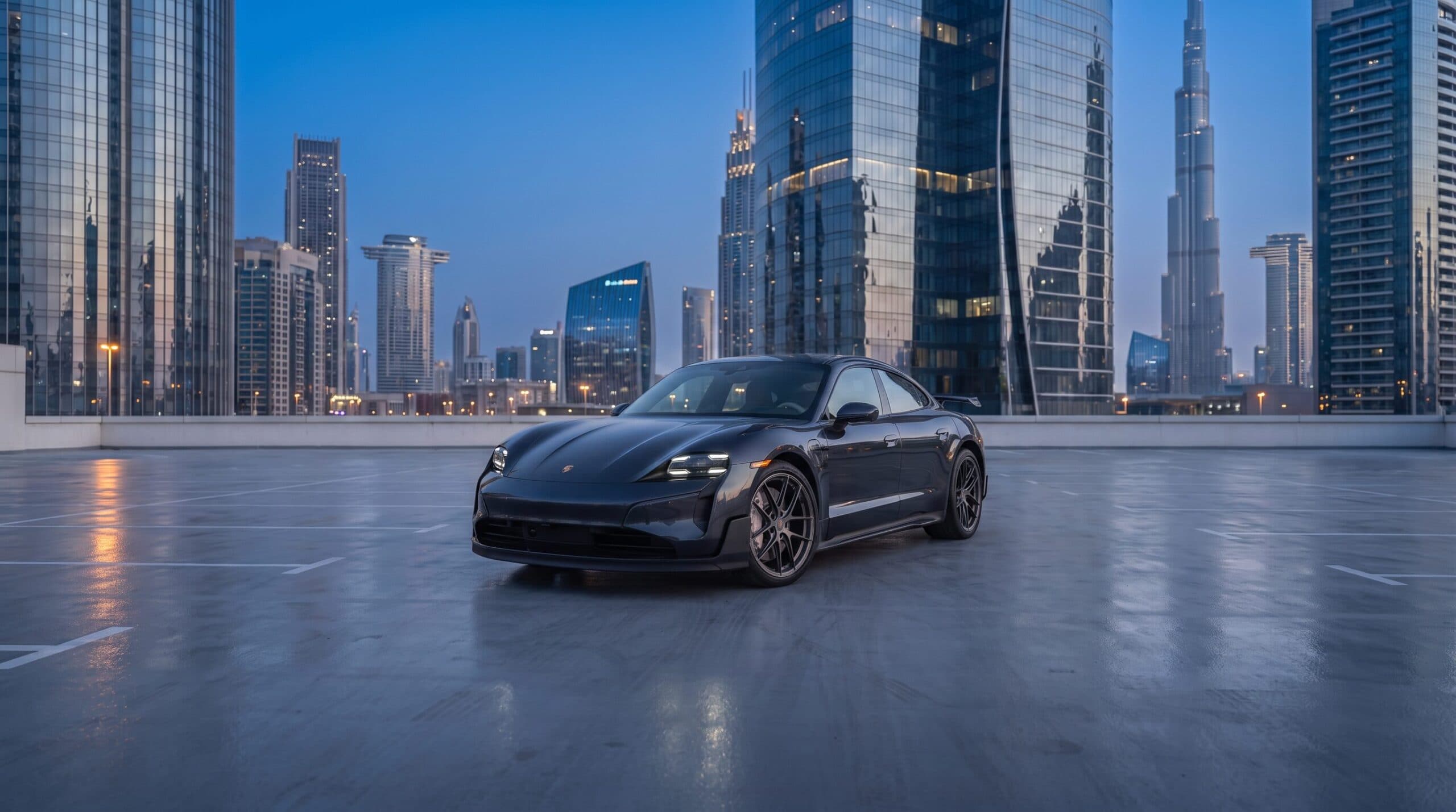 Dark grey Porsche Taycan Turbo GT on a rooftop with city towers behind it at dusk